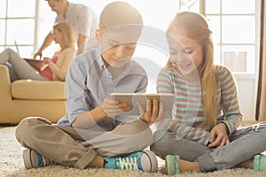 Happy siblings using digital tablet on floor with parents in background