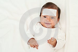 happy sick baby with cool fever pad on forehead