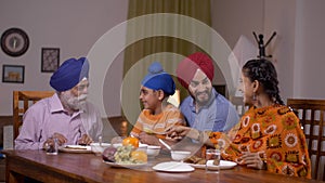 Happy Sikh Indian family eating together at home - family concept. Grandfather, father, mother, and grandson