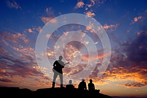 Happy silhouette friends people person having fun sitting on top of a rock hill mountain playing guitar guitarist musician , copy