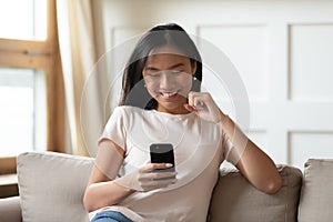 Happy sincere young asian woman looking at mobile screen.