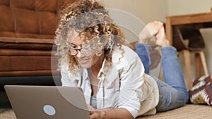 Happy single woman lay down on the floor and work with laptop smiling and having fun alone at home - concept of people and