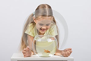 Happy six year old girl looking down on the aquarium with goldfish