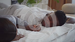 Happy sleep together. African american loving couple holding hands, sleeping in bed, man laughing, tracking shot