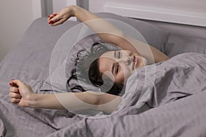 Happy sleepy girl brunette in burgundy top under grey sheets in bed. morning routine. good dream, sleeping photo