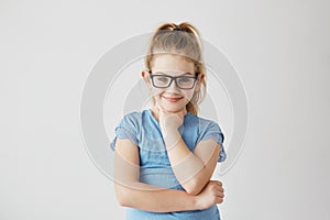 Happy small blonde girl with blue eyes looking in camera with happy and peaceful expression in brand new black glasses.
