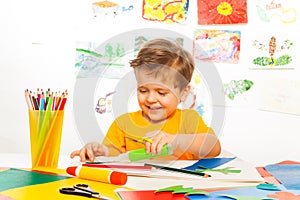 Happy small boy crafts with scissors, paper, glue