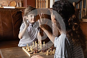 Happy small boy give high five playing chess with mom