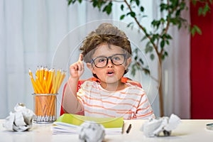 Happy small boy in glasses with finger pointing up is going to school for the first time. Child with school bag and book