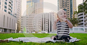 Happy small child sitting in grass with white daisies city background
