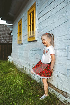 Small girl in traditional skirt posing in traditional village with wooden cottages