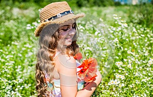 Happy small girl with beauty look wear sun hat on long curly blonde hair holding poppy flowers on natural sunny summer