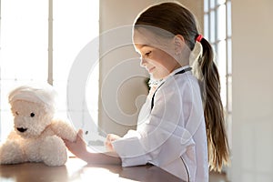 Happy small girl in medical uniform making prick to toy.