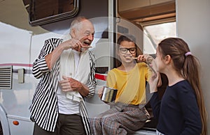 Happy small girls with grandfather brushing teeth by caravan, family holiday trip.