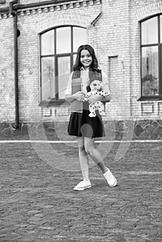 Happy small kid in school uniform hold books and toy dog in schoolyard, homework club