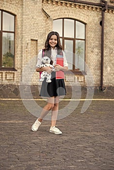 Happy small kid in school uniform hold books and toy dog in schoolyard, homework club