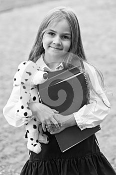 Happy small kid in school uniform hold study books and toy dog friend, friendship