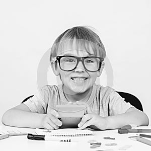 Happy smart boy in big glasses, sits at desk, looking to camera. Education. Kids idea. Genius. Back to school. Funny child in glas