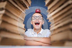 Happy smart boy in glasses sitting between two piles of books with red apple on head and look at camera smiling with