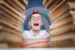 Happy smart boy in glasses sitting between two piles of books wi