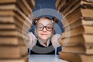 Happy smart girl in rounded glasses sitting between two piles of