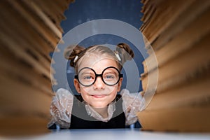 Happy smart girl in rounded glasses sitting between two piles of