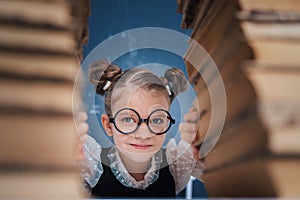 Happy smart girl in rounded glasses sitting between two piles of