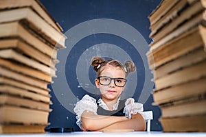 Happy smart girl in rounded glasses sitting between two piles of