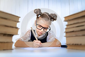 Happy smart girl in rounded glasses, writing, drawing while sitting between two piles of books