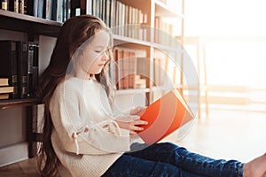 Happy smart schoolgirl reading books in library or at home