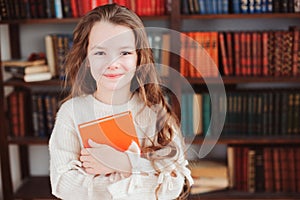 happy smart schoolgirl reading books in library or at home