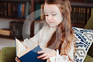 Happy smart schoolgirl reading books in library or at home