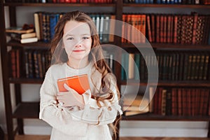 Happy smart schoolgirl reading books in library or at home