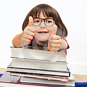 Happy smart young child with thumbs up leaning on books, indoor