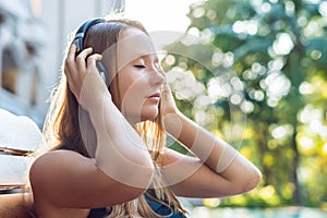 Happy smartphone woman relaxing near swimming pool listening with earbuds to streaming music. Beautiful girl using her mobile phon