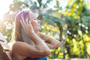 Happy smartphone woman relaxing near swimming pool listening with earbuds to streaming music. Beautiful girl using her mobile phon