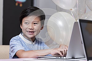 Happy smile Asean boy using laptop computer to study online e-learning from living room decorate party holiday at home