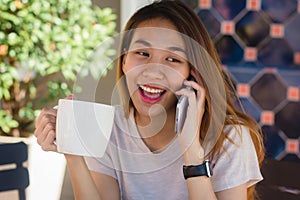 Happy smile asian business women using talking cell phone sitting in cafe and holding a cup of coffee.