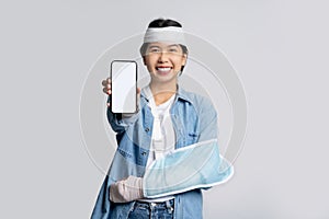 Happy smile asian woman put on soft splint and showing a smartphone white screen mockup to the camera isolated on white background