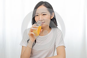 Happy smile asian young woman, girl drinking fresh orange juice in a glass bottle, holding transparent glass in hand, thirsty at