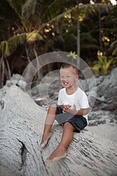 Happy smile european blond baby boy have rest and sit on white sand beach