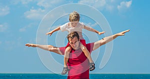 Happy smile father hugs holds on shoulders son boy male child stand blue lazur sea panorama skyline horizon in sunshine