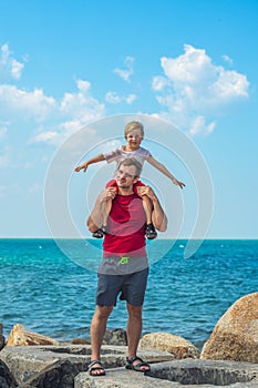 Happy smile father hugs holds on shoulders son boy male child stand blue lazur sea panorama skyline horizon in sunshine