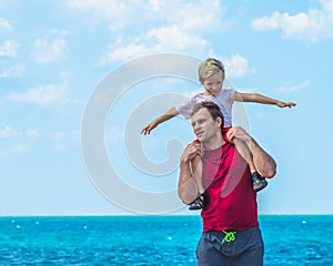 Happy smile father hugs holds on shoulders son boy male child stand blue lazur sea panorama skyline horizon in sunshine photo