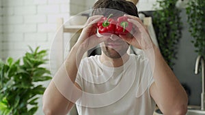 Happy smiles and plays happily with red peppers in front of his eyes in the home kitchen