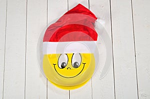 Happy smiley cartoon face on yellow paper plate and red Santa Claus hat