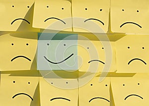 Happy smiley face on a blue sticky note surrounded by sad unhappy yellow faces