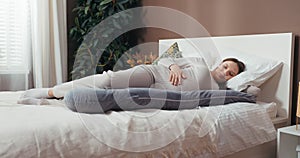 Happy smiley pregnant woman in a comfortable outfit, smiling and gently touching her belly while resting on a pregnancy