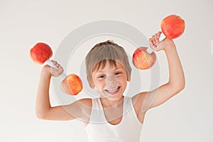 Happy smiling active strong little caucasian child in tank top lifting dumbbell made of apple during sport training workout