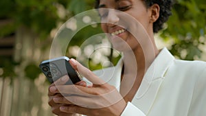 Happy smiling African American businesswoman chatting in social media with mobile app outdoors waiting meeting taxi